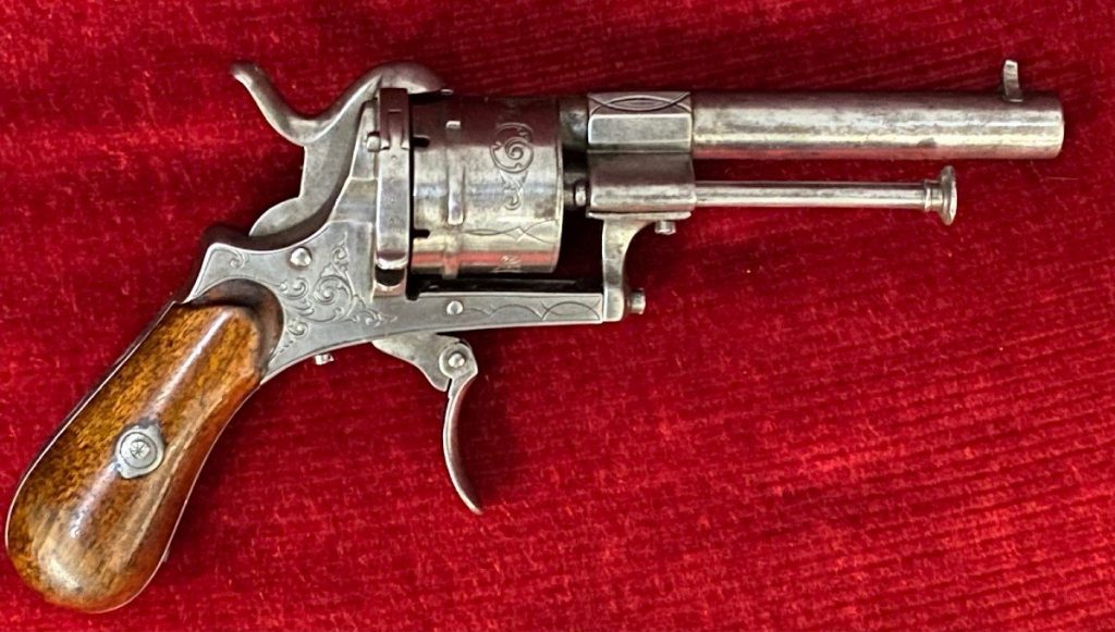 Revolver ancien en métal poli avec poignée en bois, posé sur un tissu rouge.