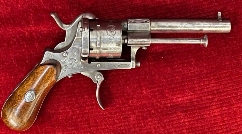Revolver ancien en métal poli avec poignée en bois, posé sur un tissu rouge.