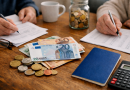 Scène intérieure montrant une personne consultant des documents financiers et des billets en euros posés sur une table, symbolisant les changements de revenus et d’épargne en début d’année.
