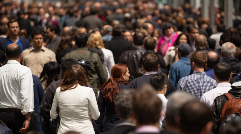 Foule dense de personnes marchant sur un trottoir urbain en pleine journée, illustrant la diversité sociale et la vie quotidienne dans une grande ville.