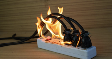 Multiprise électrique posée sur une surface en bois, avec plusieurs câbles branchés en surchauffe et des flammes visibles autour des prises.