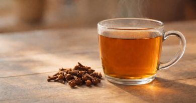 Tasse en verre remplie d’une infusion ambrée fumante, posée sur une table en bois, avec des clous de girofle entiers déposés à côté.