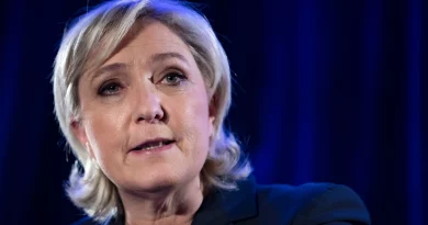 Portrait serré d’une femme politique lors d’une prise de parole publique, éclairage bleu en arrière-plan, expression sérieuse et concentrée, ambiance institutionnelle.