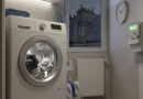 Machine à laver en fonctionnement dans une petite buanderie, avec du linge en cours de lavage, un compteur électrique mural visible et une fenêtre donnant sur des toits urbains, illustrant la consommation énergétique domestique.
