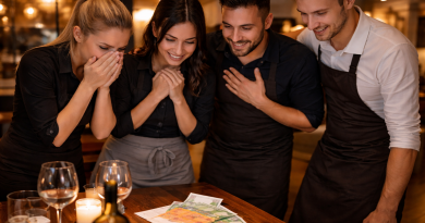 Groupe de serveurs réunis autour d’une table en bois, visiblement émus et souriants, observant une importante somme d’argent déposée devant eux dans un restaurant à l’ambiance chaleureuse.