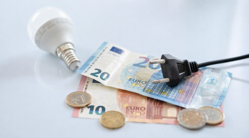 Ampoule LED, prise électrique et billets en euros posés sur une surface claire, symbolisant le coût de l’électricité et les économies d’énergie domestiques.