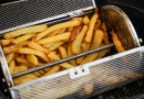 Frites dorées en cours de cuisson dans un panier métallique à mailles, placé horizontalement dans un appareil de cuisson à air chaud.