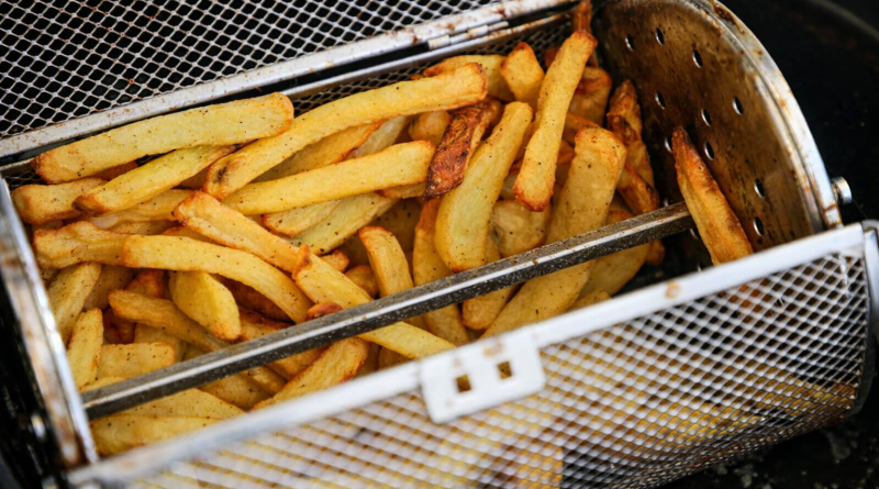 Frites dorées en cours de cuisson dans un panier métallique à mailles, placé horizontalement dans un appareil de cuisson à air chaud.
