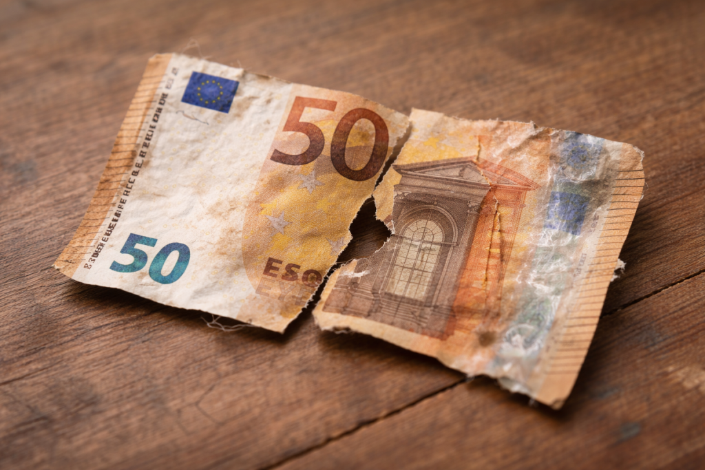 Billet de banque en euros très abîmé, fortement déchiré en plusieurs morceaux, froissé et usé, posé sur une surface en bois.