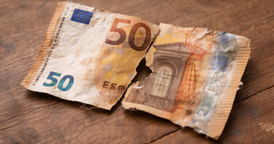 Billet de banque en euros très abîmé, fortement déchiré en plusieurs morceaux, froissé et usé, posé sur une surface en bois.