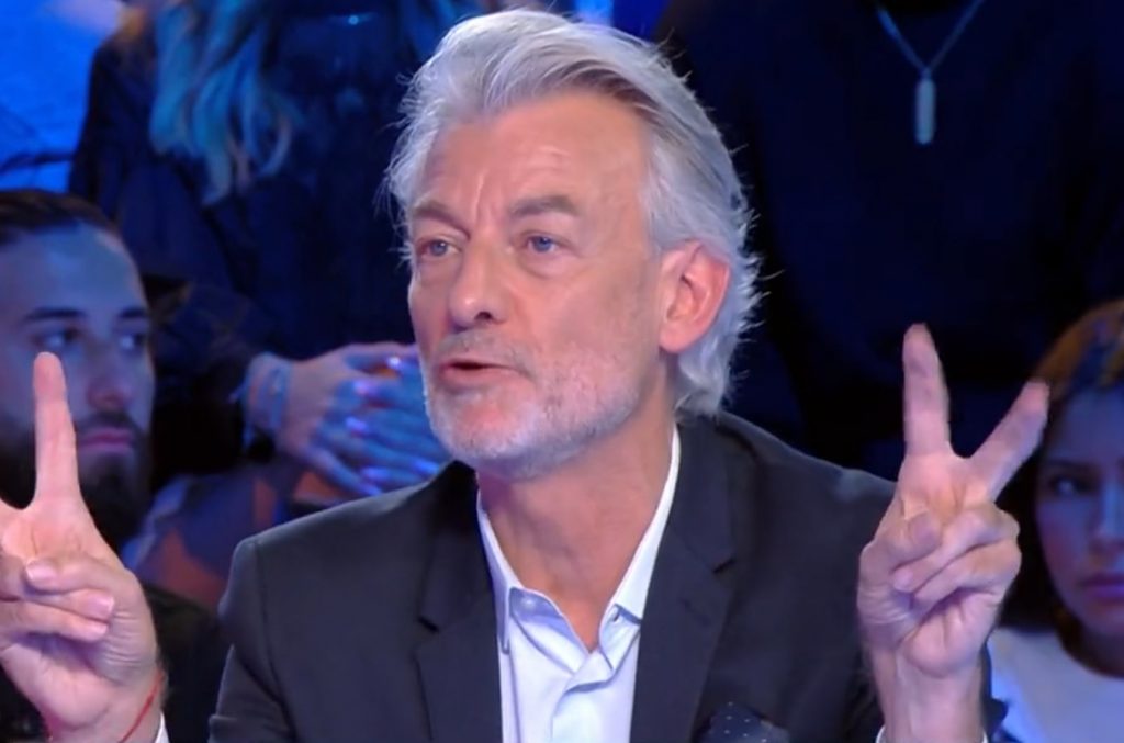 chroniqueur de télévision en plateau levant les deux mains avec un geste de citation devant un public attentif