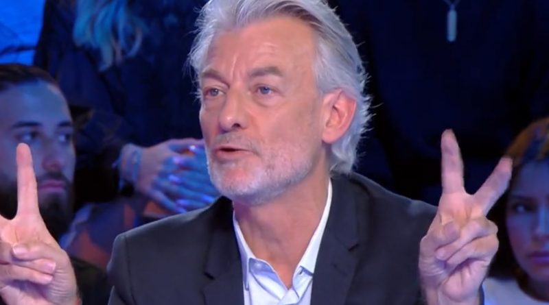 chroniqueur de télévision en plateau levant les deux mains avec un geste de citation devant un public attentif