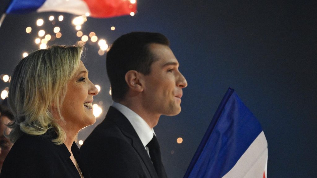 Deux responsables politiques français de profil, debout lors d’un rassemblement nocturne, tenant un drapeau tricolore avec des lumières en arrière-plan