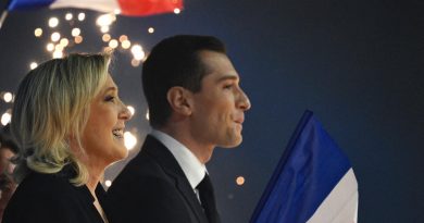 Deux responsables politiques français de profil, debout lors d’un rassemblement nocturne, tenant un drapeau tricolore avec des lumières en arrière-plan