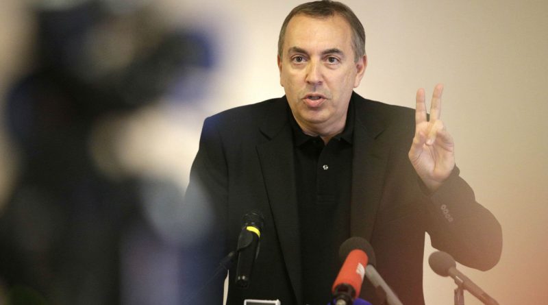 homme s’exprimant devant des microphones lors d’une conférence de presse, levant deux doigts