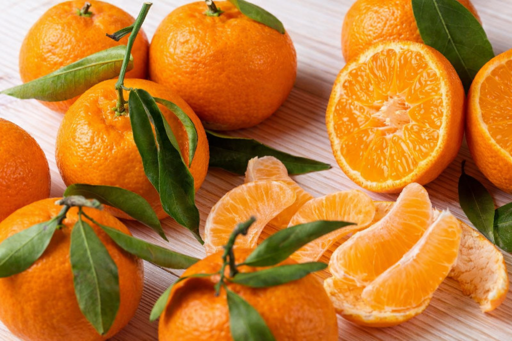 Fruits agrumes orange disposés sur une surface claire, avec plusieurs fruits entiers et des quartiers épluchés montrant une chair juteuse et brillante.