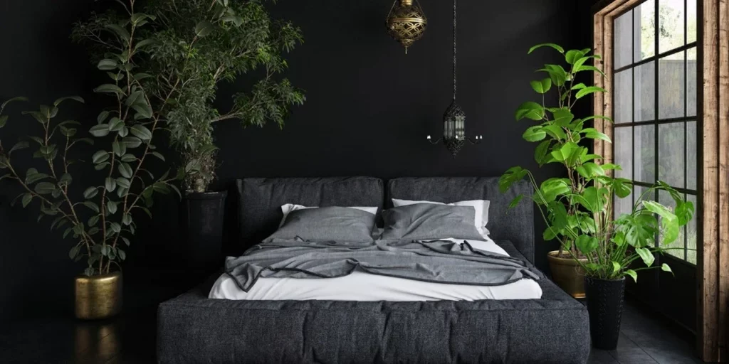 Chambre à coucher sombre avec un lit double aux draps gris, entouré de plantes vertes et éclairé par une lumière douce créant une ambiance calme et apaisante.
