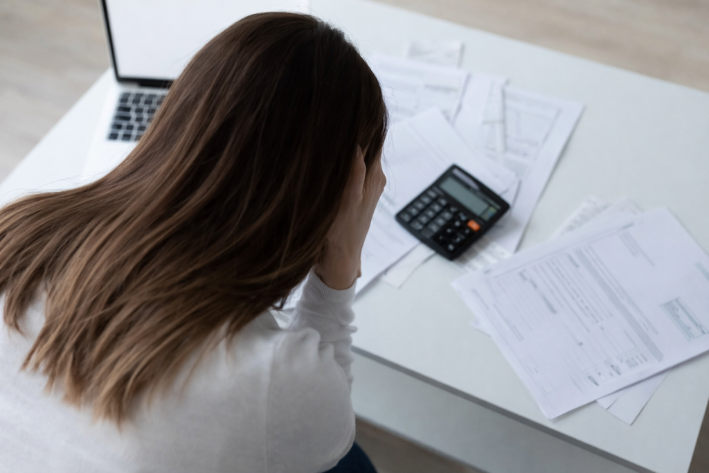 personne assise à un bureau examinant des documents financiers avec une calculatrice, exprimant une situation de tension budgétaire