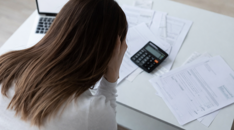 personne assise à un bureau examinant des documents financiers avec une calculatrice, exprimant une situation de tension budgétaire