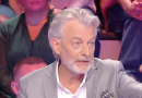 Chroniqueur à la barbe grise s’exprimant avec fermeté sur un plateau de télévision, main levée, visage concentré, public visible en arrière-plan sous un éclairage de studio.