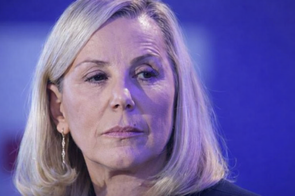 Portrait serré d’une journaliste de télévision au regard sérieux, éclairée par une lumière bleutée sur un plateau de chaîne d’information.