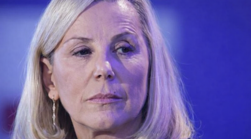 Portrait serré d’une journaliste de télévision au regard sérieux, éclairée par une lumière bleutée sur un plateau de chaîne d’information.