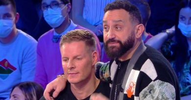 deux animateurs de télévision assis côte à côte sur un plateau, l’un posant une main sur l’épaule de l’autre, sous les projecteurs, avec un public en arrière-plan