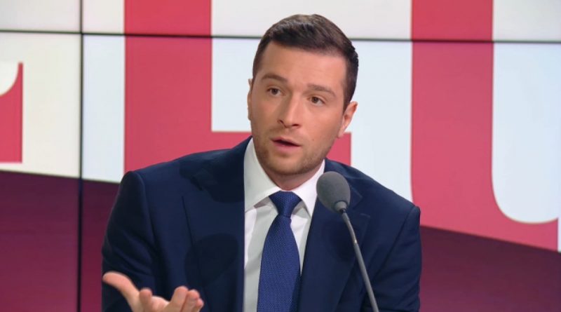 homme politique en costume s’exprimant derrière un pupitre avec un micro, décor graphique rouge en arrière-plan