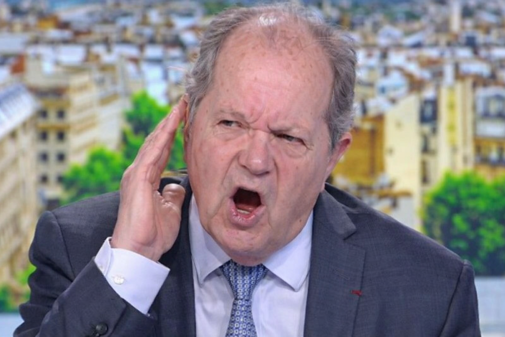 Animateur de télévision en colère sur un plateau d’actualité, main levée près de l’oreille, expression tendue lors d’un débat diffusé en direct