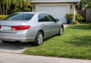 Voiture garée partiellement sur une pelouse résidentielle entourée de végétation verte.