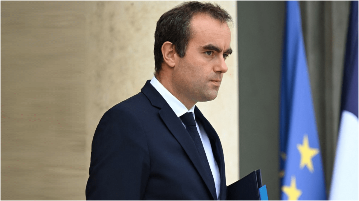 Responsable politique en costume sombre marchant à l’extérieur d’un bâtiment officiel avec des drapeaux en arrière-plan