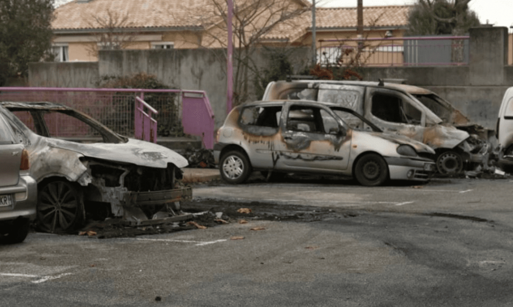 Plusieurs voitures calcinées et fortement endommagées après un incendie survenu dans un parking à ciel ouvert.