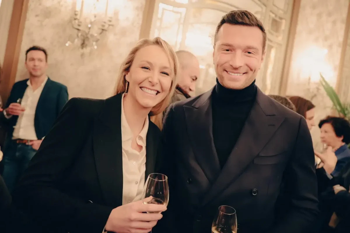 deux personnalités souriantes posant ensemble lors d’une réception élégante avec des verres à la main