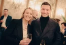 deux personnalités souriantes posant ensemble lors d’une réception élégante avec des verres à la main