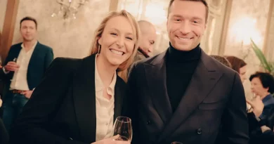 deux personnalités souriantes posant ensemble lors d’une réception élégante avec des verres à la main