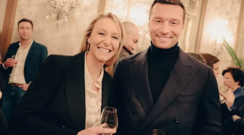 deux personnalités souriantes posant ensemble lors d’une réception élégante avec des verres à la main