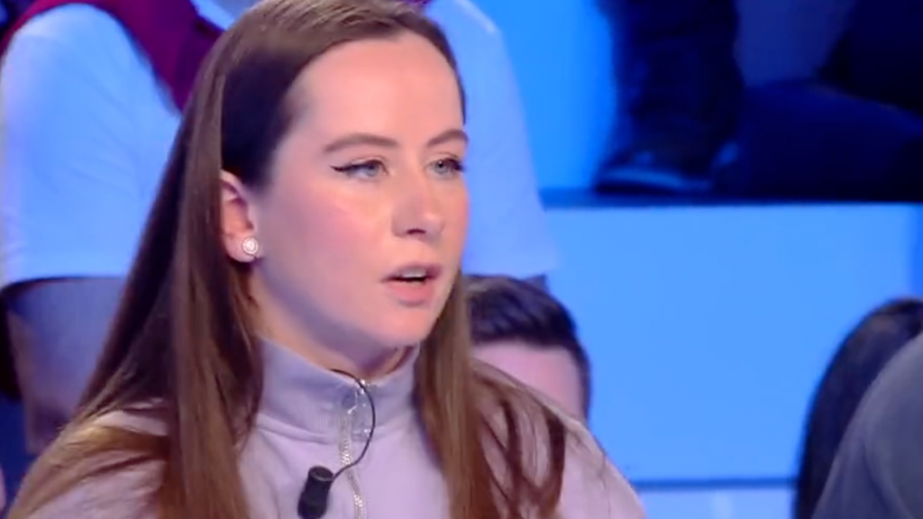 Jeune femme s’exprimant sur un plateau télévisé, visage sérieux, regard tourné vers un interlocuteur, ambiance de débat public sous éclairage bleu.