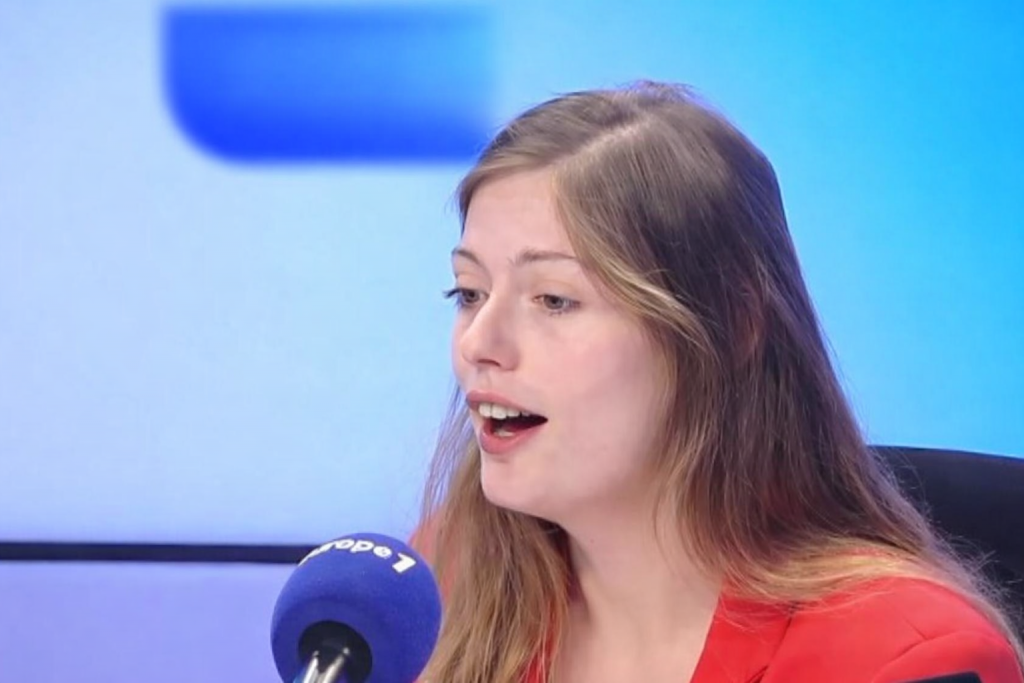 Jeune femme s’exprimant dans un studio radio, micro devant elle, regard concentré, ambiance bleutée, illustrant une polémique politique et sociétale en France.