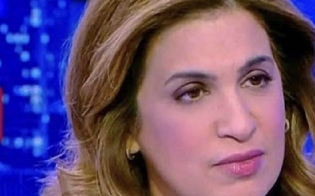Journaliste femme en plateau de télévision, expression sérieuse et concentrée, éclairage bleu d’un studio d’actualité, ambiance tendue, cadrage serré sur le visage