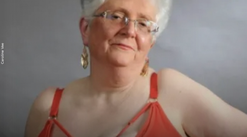 Femme âgée aux cheveux gris courts portant de la lingerie rouge, regard calme et assumé face à l’objectif, posture droite, expression sereine, fond neutre