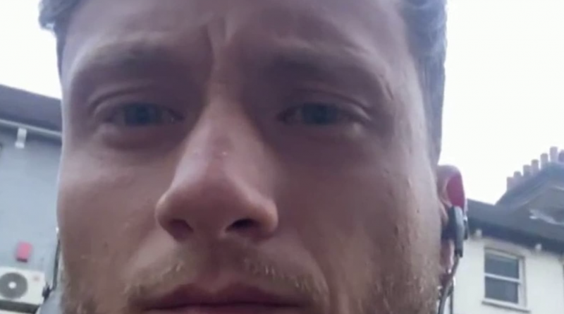 Gros plan sur le visage d’un homme à l’expression grave, filmé en extérieur dans une rue résidentielle, avec des maisons en arrière-plan et un écouteur sans fil visible à l’oreille.