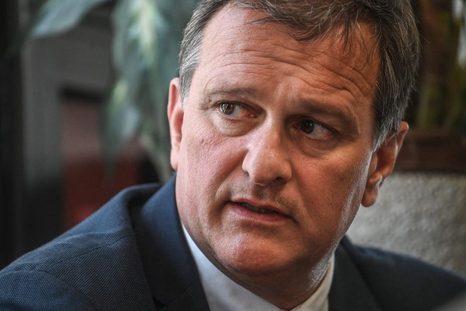 Portrait rapproché d’un homme politique français en costume sombre et chemise claire, regard tourné vers la gauche, expression sérieuse, dans un cadre intérieur avec arrière-plan flou.