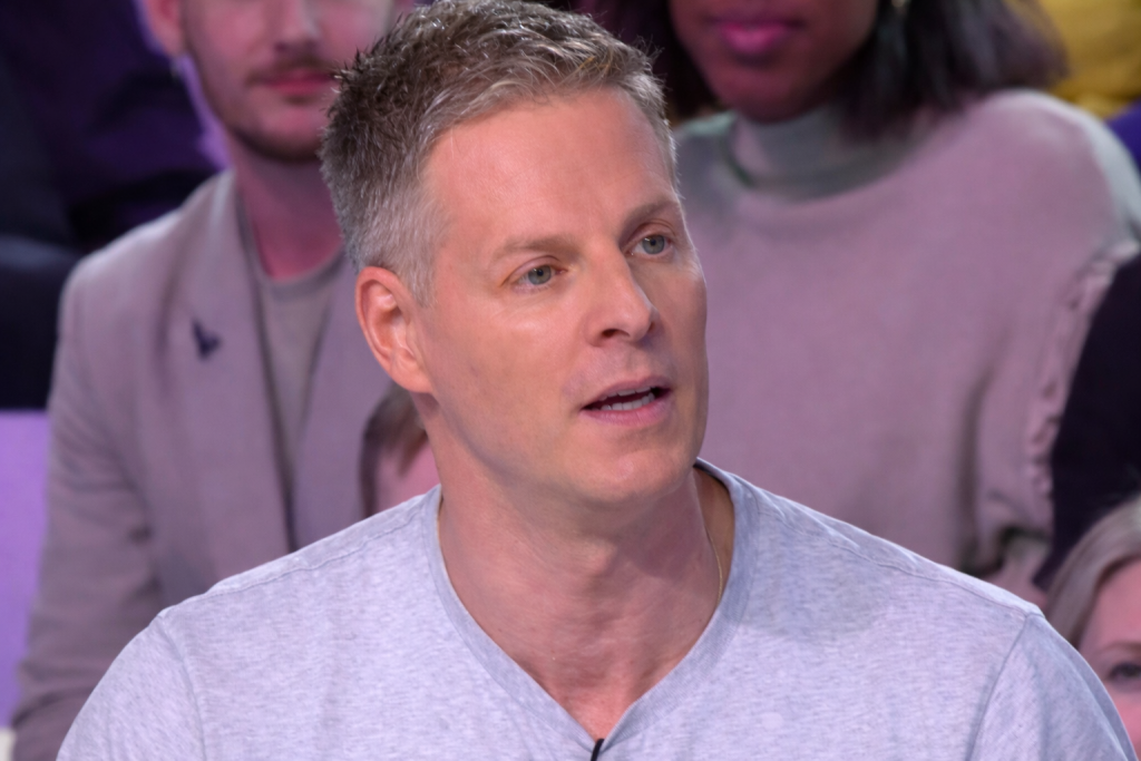 Chroniqueur de télévision assis sur un plateau, parlant face au public, éclairage de studio et ambiance de débat médiatique