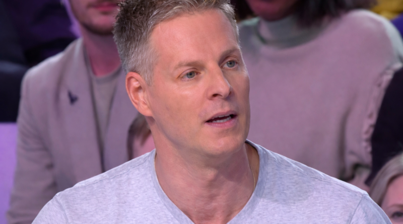 Chroniqueur de télévision assis sur un plateau, parlant face au public, éclairage de studio et ambiance de débat médiatique