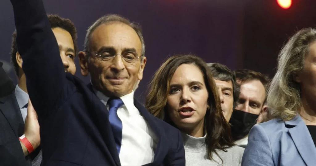 Un groupe de responsables politiques réunis sur une scène, l’un d’eux levant le bras devant une foule, dans une ambiance de meeting.