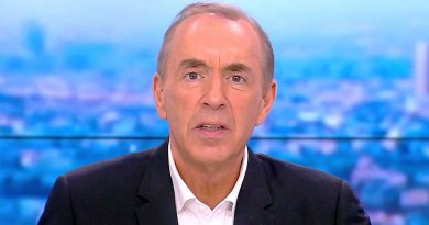 Présentateur masculin en costume sombre et chemise blanche, regard sérieux face caméra, en plateau de chaîne d’information avec arrière-plan flouté aux tons bleus représentant une ville.