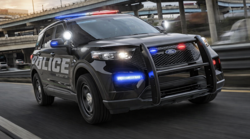 Véhicule de police noir équipé de gyrophares rouges et bleus allumés circulant rapidement sur une autoroute urbaine, avec échangeurs routiers en béton et circulation floutée en arrière-plan.