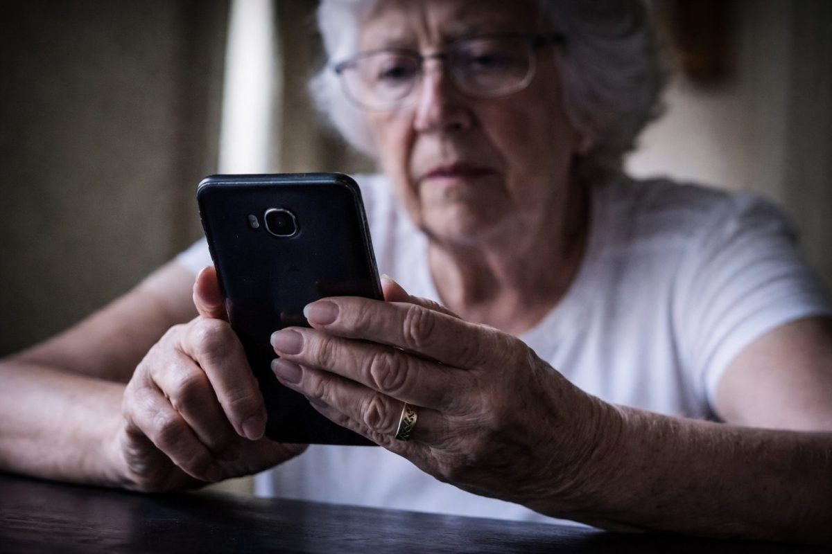Personne âgée tenant un smartphone et regardant l’écran avec inquiétude, illustrant les appels indésirables et le démarchage téléphonique abusif