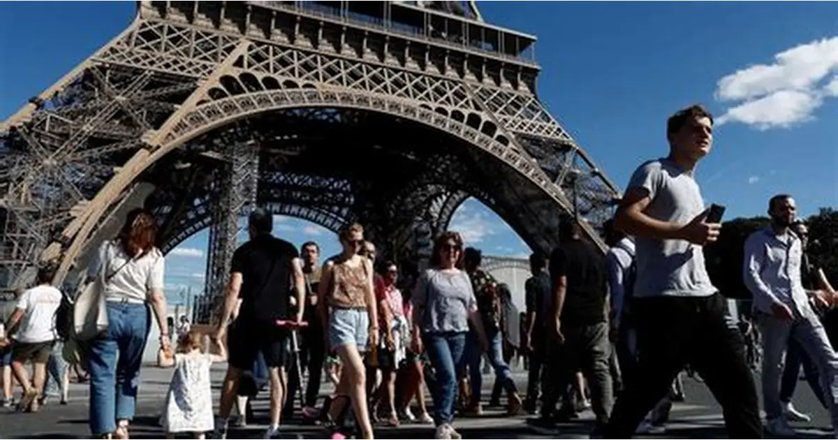 foule de touristes marchant sous une grande tour métallique emblématique dans une grande ville européenne, avec des visiteurs prenant des photos et se promenant dans une zone touristique très fréquentée