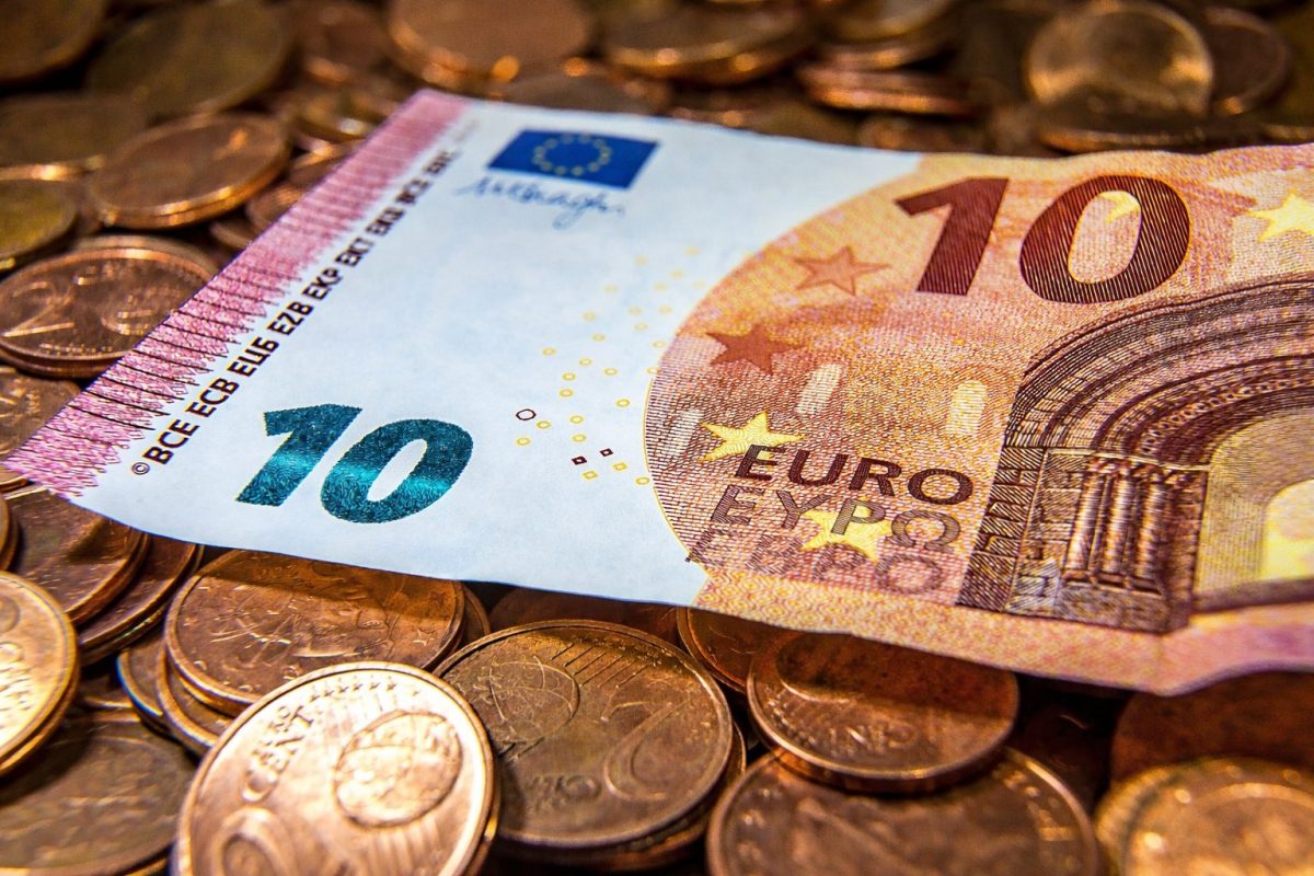 Billet de dix euros posé sur un tas de pièces de monnaie en euro, illustrant le débat sur les aides sociales et le minimum vieillesse en France.